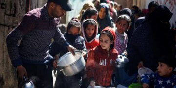 Palestinian children wait to receive food cooked by a charity kitchen amid famine, in Rafah, in the southern Gaza Strip on March 5, 2024 [Reuters/Mohammed Salem]