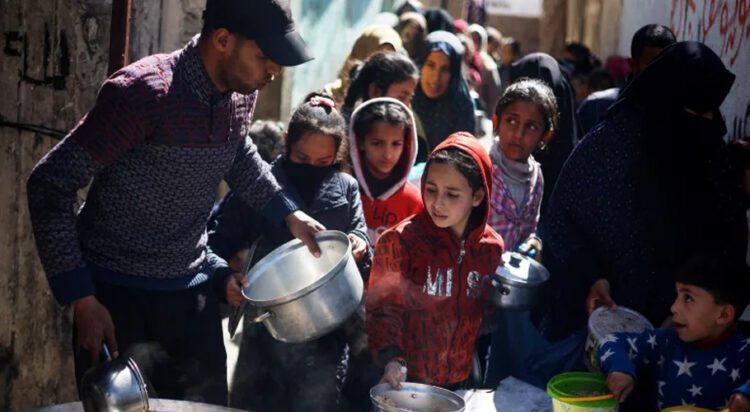 Palestinian children wait to receive food cooked by a charity kitchen amid famine, in Rafah, in the southern Gaza Strip on March 5, 2024 [Reuters/Mohammed Salem]