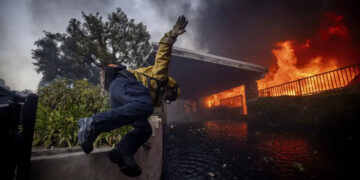 A firefighter jumps over a fence while fighting the Palisades Fire in the Pacific Palisades neighborhood of Los Angeles, Tuesday, Jan. 7, 2025. (AP Photo/Ethan Swope)