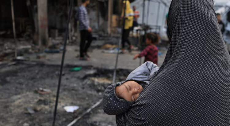 A Palestinian woman holds a child, as Palestinians inspect the damage at a school sheltering displaced people, following an Israeli strike, in Gaza City, April 23, 2025. REUTERS/Dawoud Abu Alkas