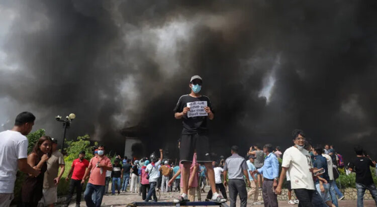 A demonstrator holds a sign as smoke rises at the parliament complex during a curfew in Kathmandu [Adnan Abidi/Reuters]