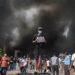 A demonstrator holds a sign as smoke rises at the parliament complex during a curfew in Kathmandu [Adnan Abidi/Reuters]