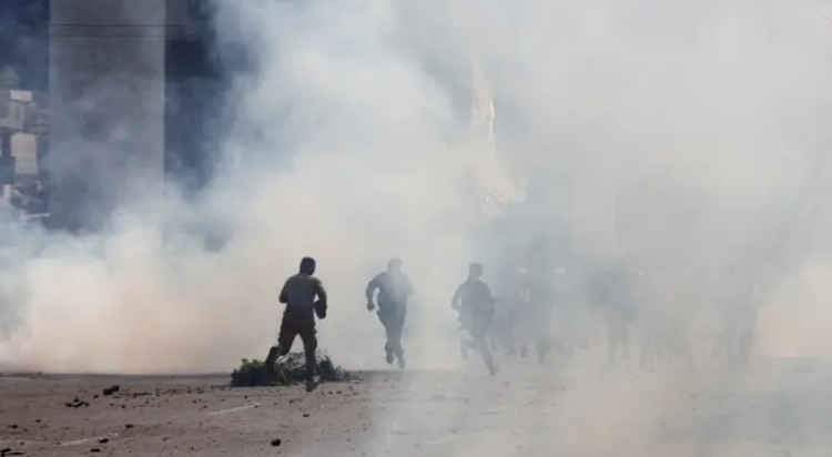 Police officers and supporters of Tehreek-e-Labbaik Pakistan (TLP) run amid tear gas fired by police during a solidarity march for Gaza in Lahore on October 10. — Reuters