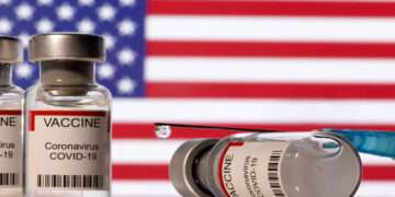 Vials labelled "VACCINE Coronavirus COVID-19" and a syringe are seen in front of a displayed U.S. flag in this illustration taken December 11, 2021. REUTERS/Dado Ruvic/Illustration