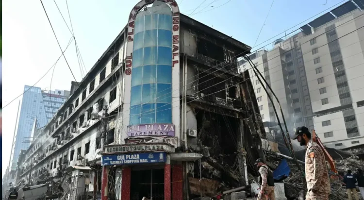 Paramilitary personnel walk past charred remains of the Gul Plaza shopping mall in Karachi on Jan 22, 2026. — AFP